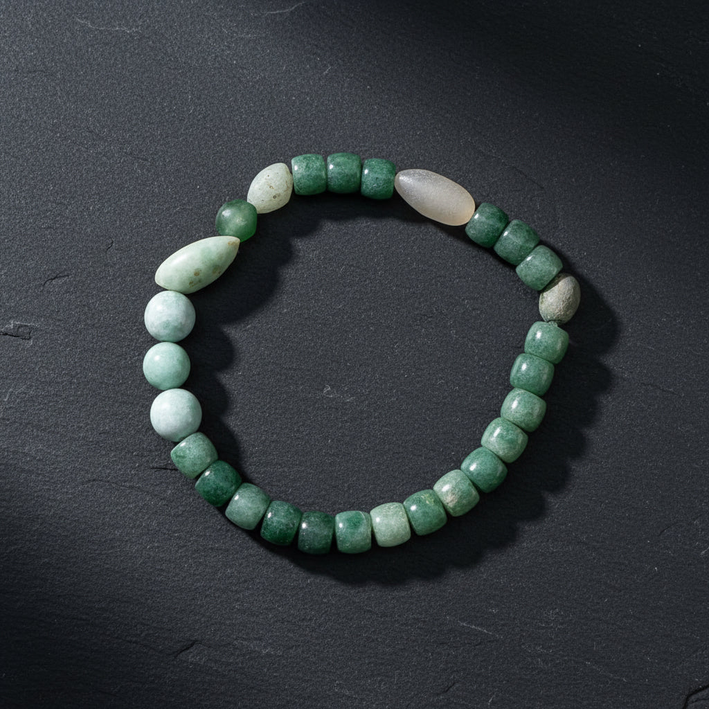 A beaded stretch bracelet made of green stone beads and two pale white beads, displayed on a weathered wood surface.
