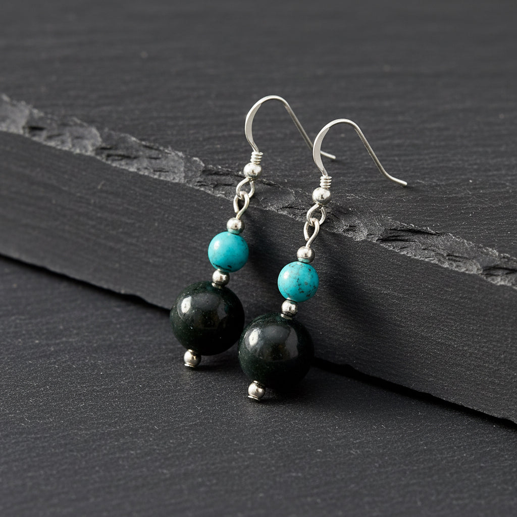 A pair of dangle earrings featuring large dark green polished beads, smaller turquoise blue beads, and silver fishhook wires, shown against a plain white background.