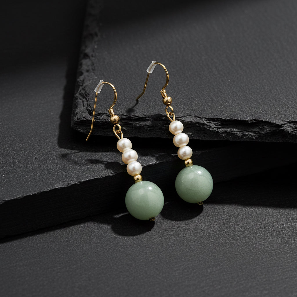 A pair of drop earrings featuring white freshwater pearls, small gold spacer beads, and a large light green jadeite bead dangle, shown on a plain white background.