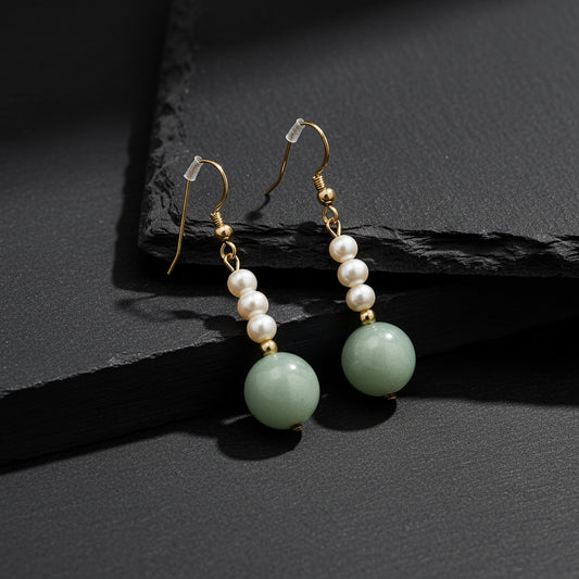 A pair of drop earrings featuring white freshwater pearls, small gold spacer beads, and a large light green jadeite bead dangle, shown on a plain white background.