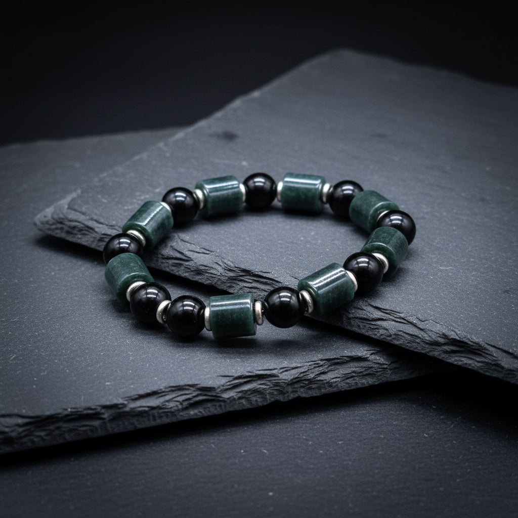 A beaded stretch bracelet made of dark green and black stone beads, displayed on a piece of natural wood with moss in the background. A watermark for 'luki lapidary' is visible in the bottom-left corner.