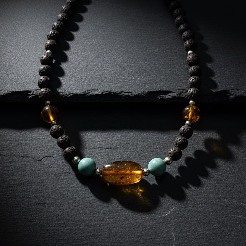 A handmade beaded necklace featuring dark brown lava stones, translucent amber beads, and light blue turquoise beads, displayed on a weathered gray wooden surface. A watermark for 'luki lapidary' is visible in the bottom right corner.