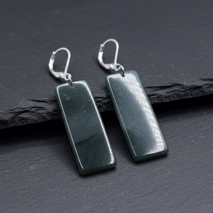 A pair of rectangular dark gray stone drop earrings with silver leverback hooks, displayed on a piece of weathered wood outdoors.