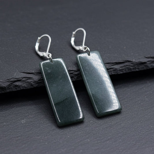 A pair of rectangular dark gray stone drop earrings with silver leverback hooks, displayed on a piece of weathered wood outdoors.