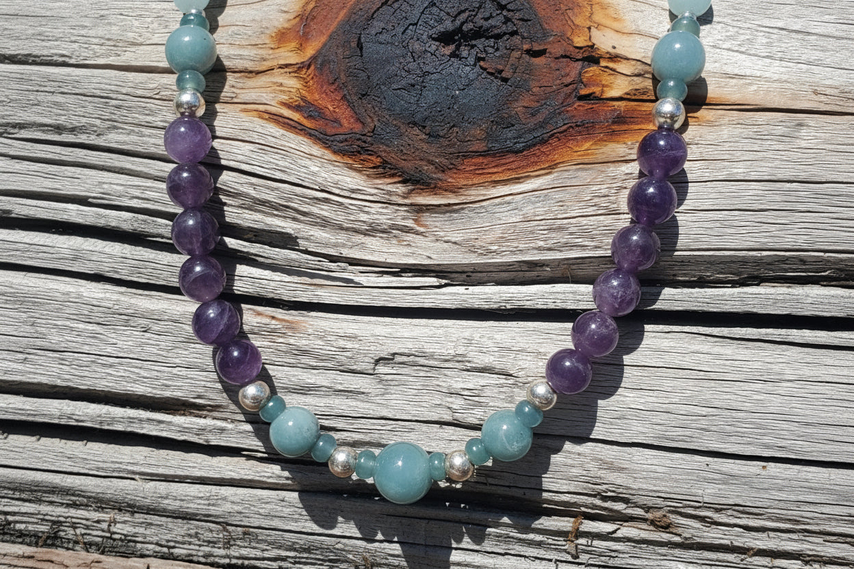 A beaded necklace made of purple amethyst, light blue jade, and small silver spacer beads, displayed on a weathered wooden surface.