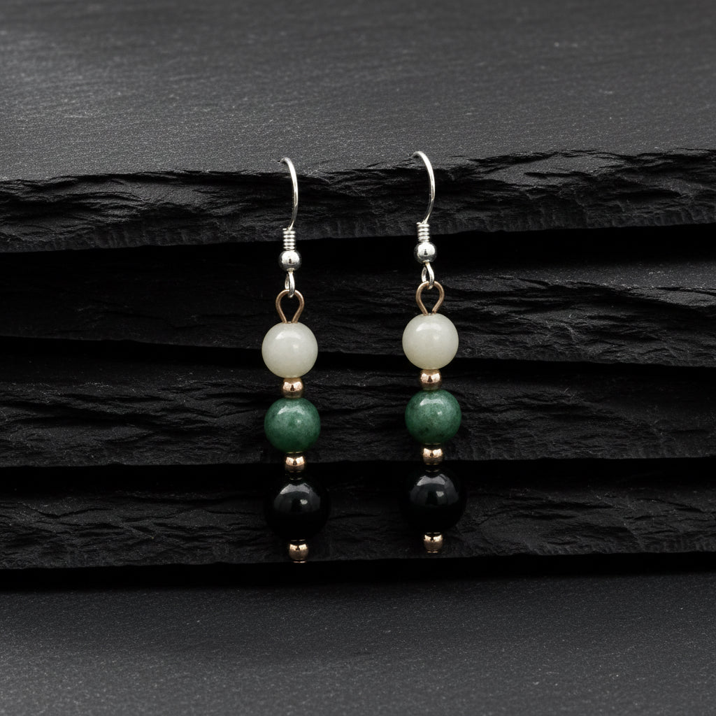 A pair of dangle earrings with three stacked round beads on each earring. The beads are white, green, and black, separated by small rose gold spacer beads, hanging from silver fishhook wires on a plain white background.