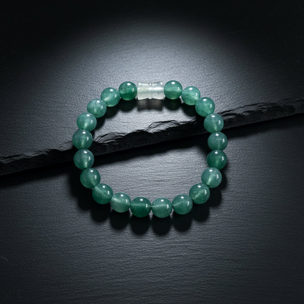 A beaded bracelet made of round, polished dark green stone beads with a small clear plastic spacer, displayed on a textured gray wood background.