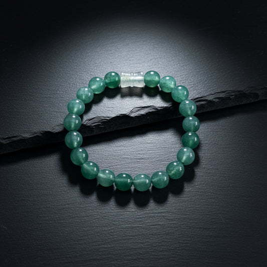 A beaded bracelet made of round, polished dark green stone beads with a small clear plastic spacer, displayed on a textured gray wood background.