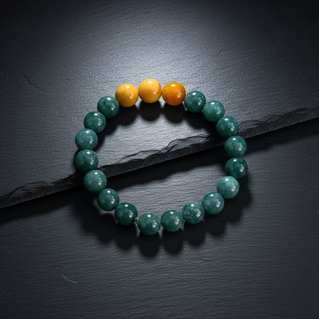 A beaded stretch bracelet made of dark green marbled beads with three smooth orange-yellow accent beads at the top, displayed on a rustic gray wood background.