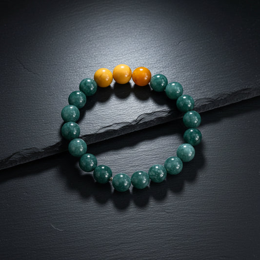 A beaded stretch bracelet made of dark green marbled beads with three smooth orange-yellow accent beads at the top, displayed on a rustic gray wood background.