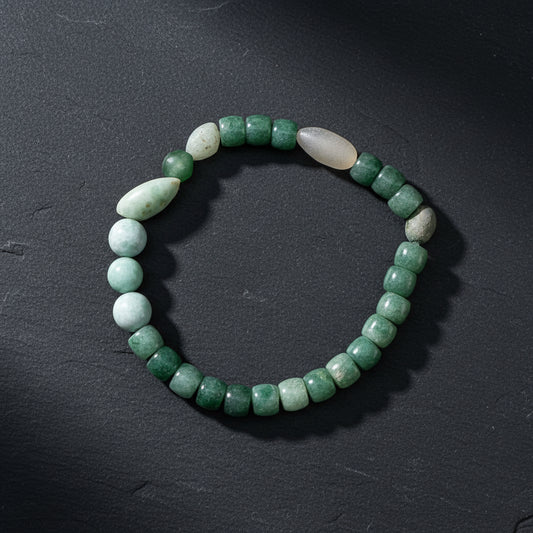 A beaded stretch bracelet made of green stone beads and two pale white beads, displayed on a weathered wood surface.