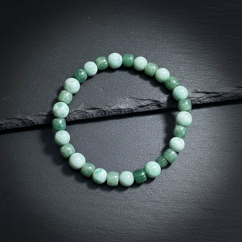 A beaded stretch bracelet made of alternating round light green and faceted dark green beads, displayed on a textured gray wood background.
