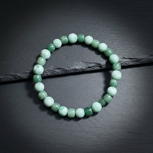 A beaded stretch bracelet made of alternating round light green and faceted dark green beads, displayed on a textured gray wood background.