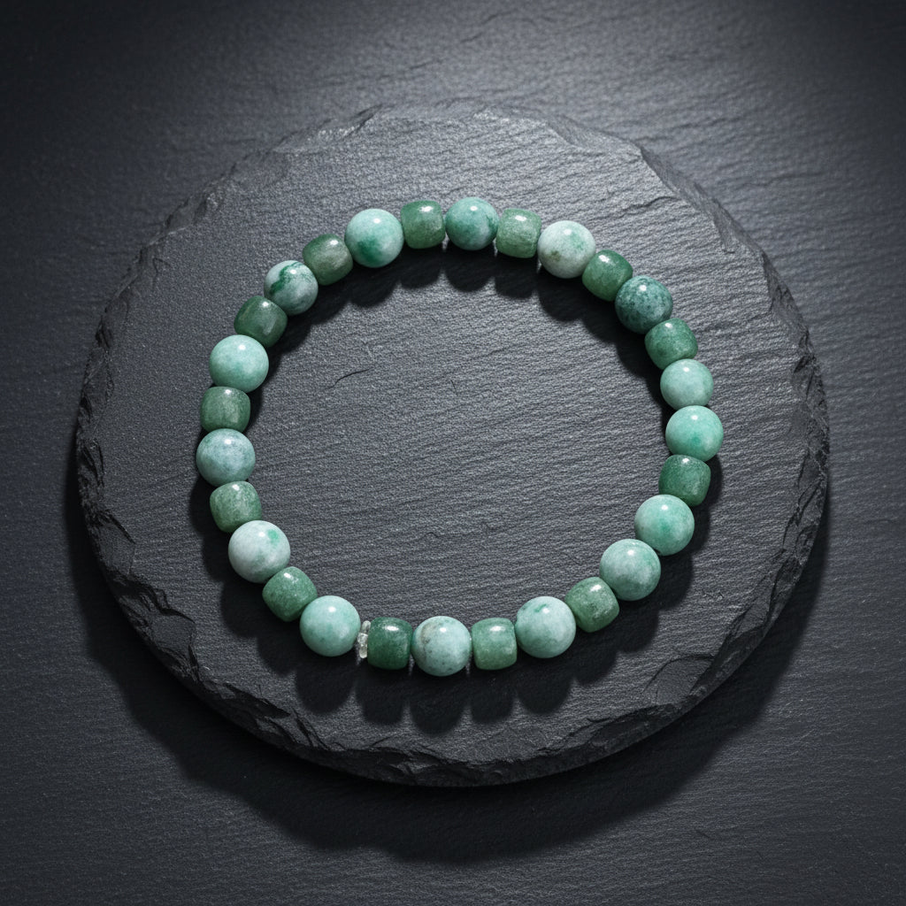 A beaded stretch bracelet made of green stone beads, including round and barrel-shaped pieces, displayed on a rustic wooden surface.