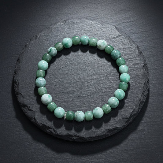A beaded stretch bracelet made of green stone beads, including round and barrel-shaped pieces, displayed on a rustic wooden surface.