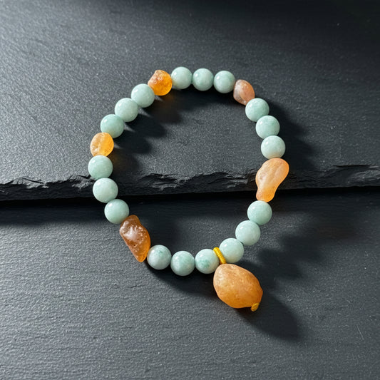 A beaded bracelet made of light blue-green round beads with several smooth, irregular orange-brown accent stones, displayed on a weathered gray wood surface.