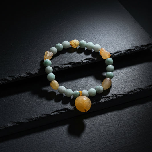 A beaded stretch bracelet featuring light blue-green stone beads, natural tan and brown stones, and a large smooth round amber-yellow bead at the bottom, displayed on a weathered gray wood surface.
