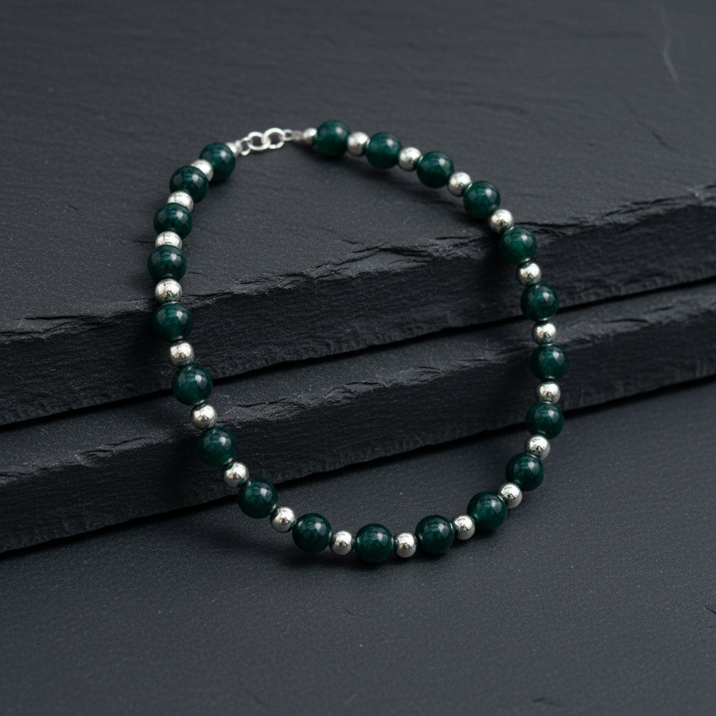 A beaded necklace with dark green faceted beads and small metallic spacer beads, displayed on a gray wood-grain surface.
