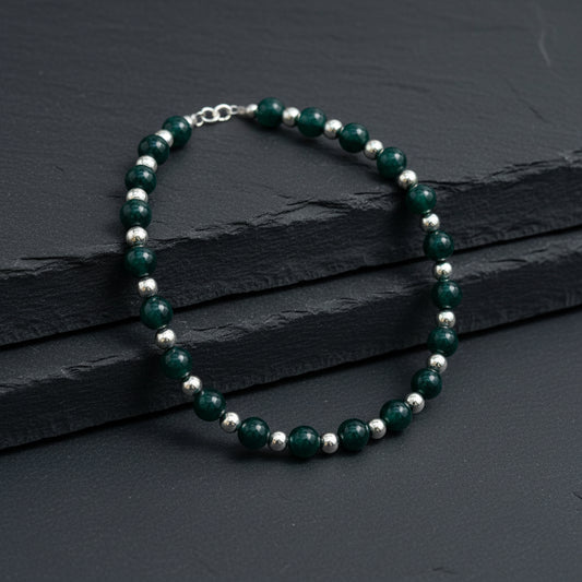 A beaded necklace with dark green faceted beads and small metallic spacer beads, displayed on a gray wood-grain surface.