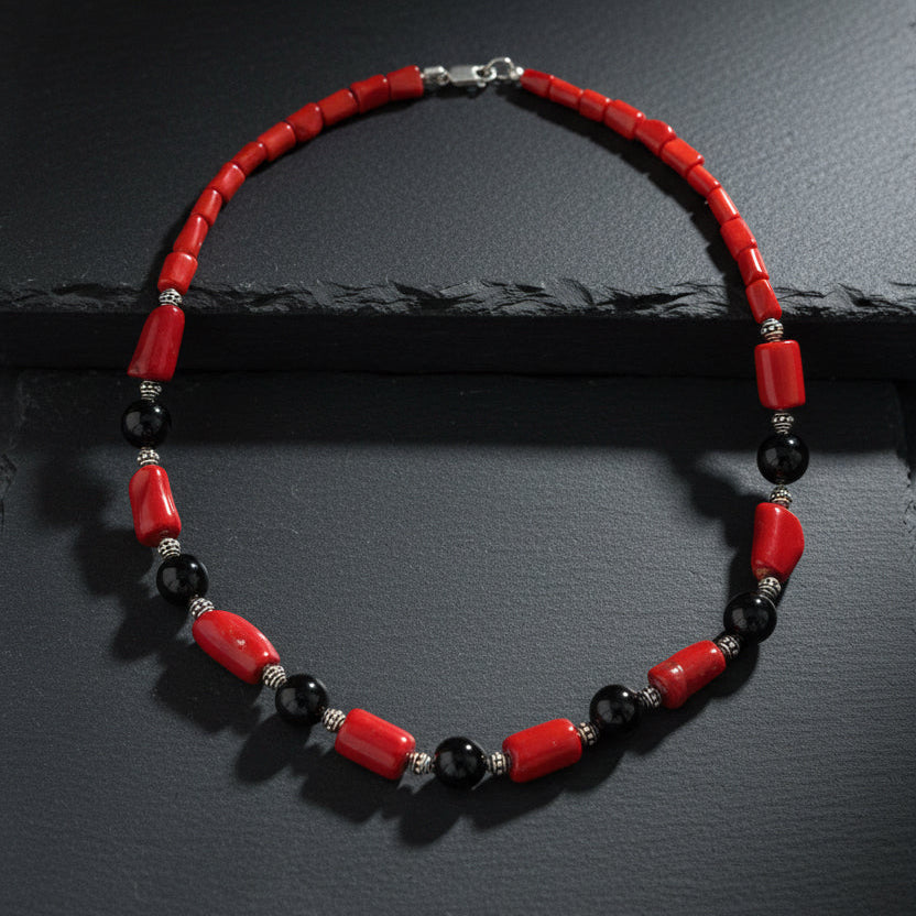 A beaded necklace with red cylindrical beads, black round beads, and small silver spacer beads, displayed on a wooden surface.