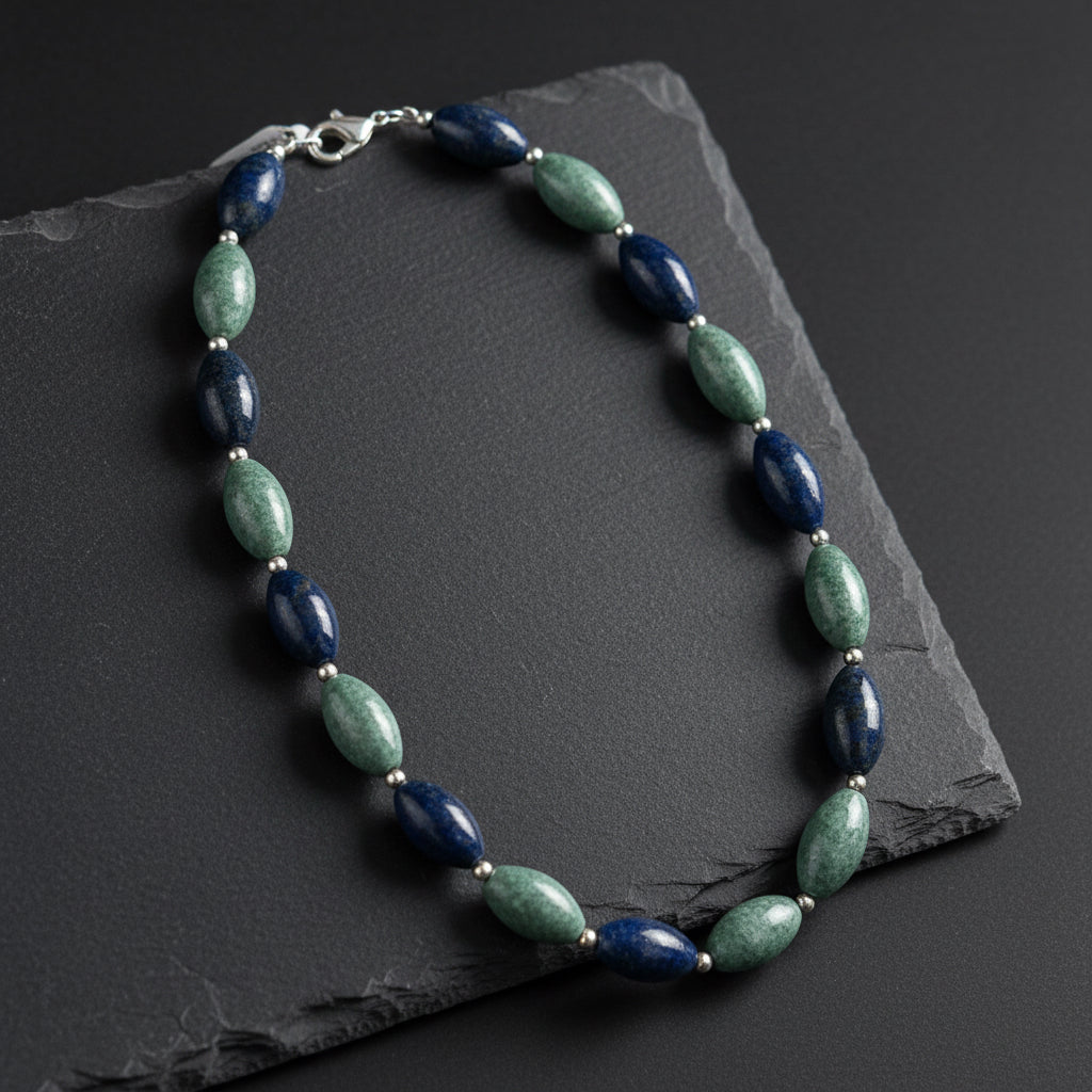 A beaded necklace with alternating dark navy blue and green stone beads, separated by small gold spacer rings, displayed on a rustic wooden surface.