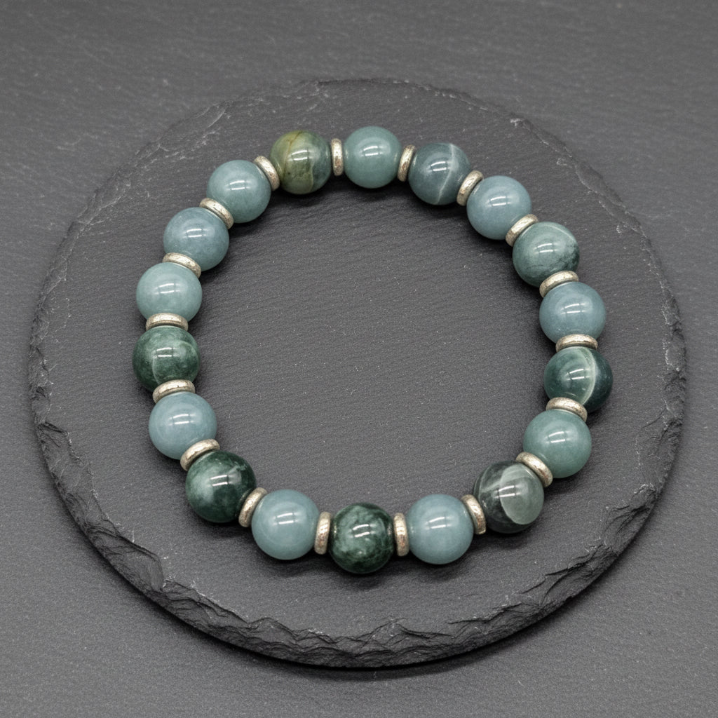 A beaded stretch bracelet made of light blue and green marbled gemstone beads separated by small metallic spacer rings, displayed on a dark gray slate surface. A watermark logo for 'luki lapidary' is visible in the bottom-left corner.